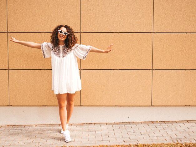 Bello modello sorridente con l'acconciatura di riccioli afro vestito in abito bianco hipster estate.