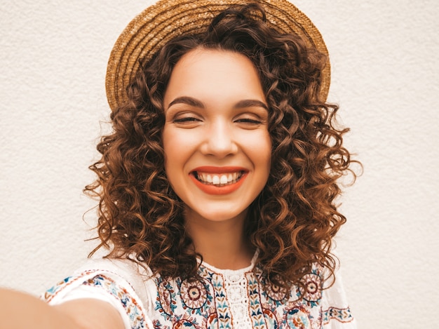 Bello modello sorridente con l'acconciatura di riccioli afro vestito in abito bianco hipster estate.