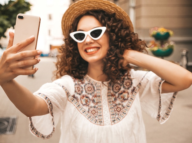 Bello modello sorridente con l'acconciatura di riccioli afro vestito in abito bianco hipster estate.