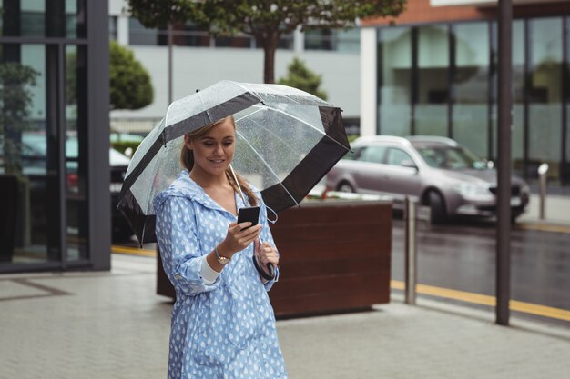 Bello ombrello della tenuta della donna mentre per mezzo del telefono cellulare