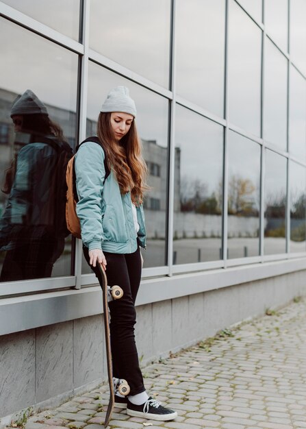 Bello pattinatore femminile che tiene il suo skateboard