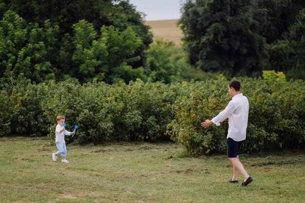 Bello ragazzo che gioca con le bolle il giorno soleggiato nel giardino.