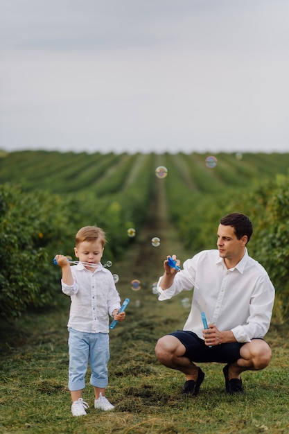 Bello ragazzo che gioca con le bolle il giorno soleggiato nel giardino.