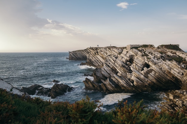 Bello scatto di una costa ricoperta di cespugli con formazioni rocciose inclinate di arenaria a Peniche