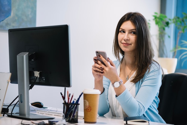 Bello smartphone di lettura rapida della donna in ufficio