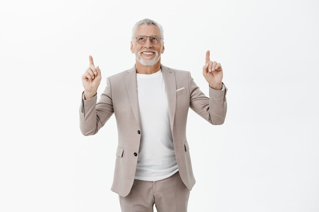 Bello sorridente vecchio uomo d'affari in tuta che punta e che osserva in su