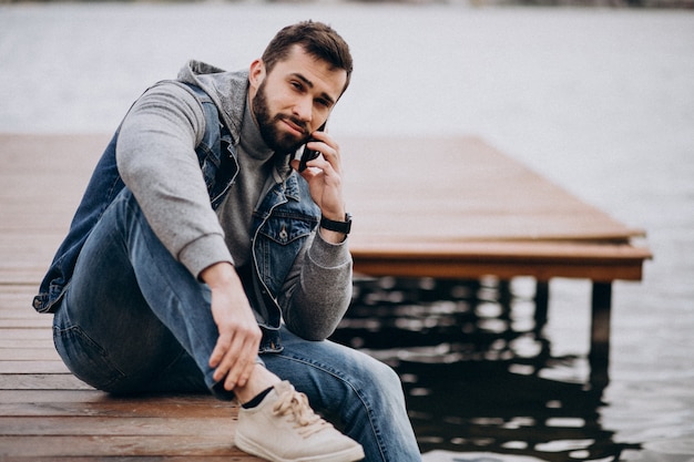 Bello uomo barbuto dal fiume nel parco seduto sul molo