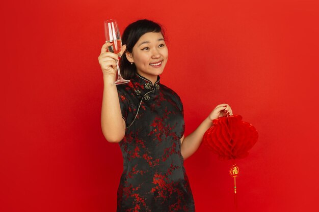 Bere champagne e tenere la lanterna. Buon Capodanno cinese. Ritratto di ragazza asiatica su sfondo rosso. Il modello femminile in abiti tradizionali sembra felice. Copyspace.