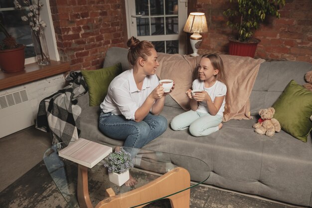 Bere il tè, parlare. Madre e figlia durante l'autoisolamento a casa durante la quarantena, il tempo in famiglia accogliente, il comfort, la vita domestica. Modelli sorridenti allegri e felici. Sicurezza, prevenzione, concetto di amore.