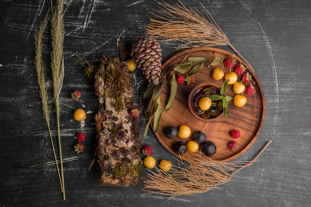 Berry mix su un piatto di legno con rami di quercia e coni da parte