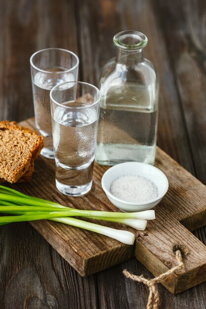 Bevanda alcolica con cipolla verde, pane tostato e sale sulla parete in legno. Bevanda alcolica pura artigianale e spuntino tradizionale. Spazio negativo. Celebrando il cibo e delizioso.