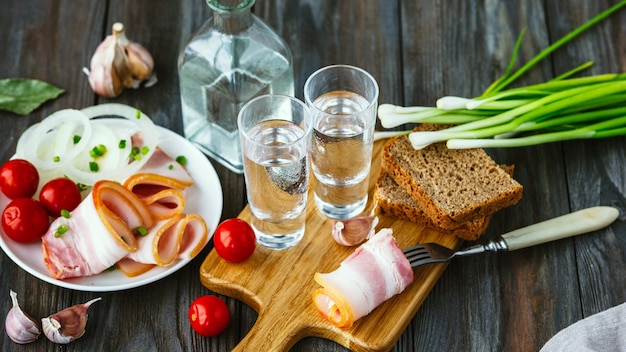 Bevanda alcolica con lardo e cipolla verde sulla parete in legno. Bevanda alcolica pura artigianale e snack tradizionali, pomodori e pane tostato. Spazio negativo. Celebrando il cibo e delizioso.