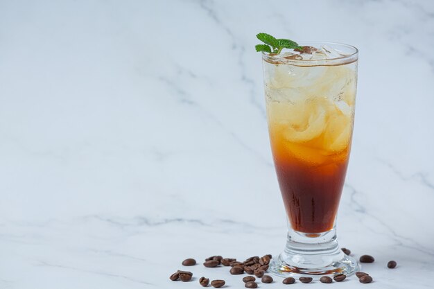 Bevanda estiva caffè ghiacciato o soda in un bicchiere sulla superficie bianca.