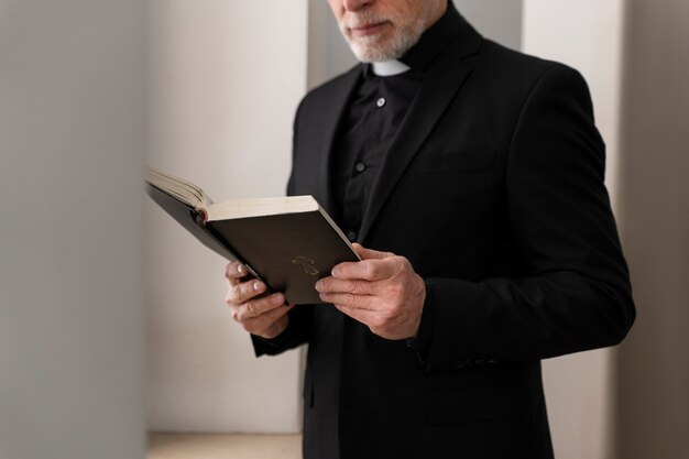 Bibbia della lettura del sacerdote anziano di vista laterale