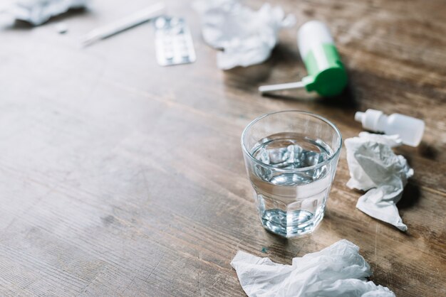 Bicchiere d&#39;acqua; carta velina stropicciata e medicinali su fondali in legno