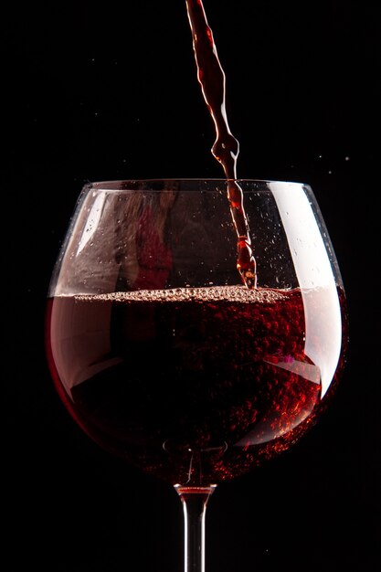 Bicchiere da vino vista frontale che viene versato con vino rosso su bevanda alcolica di Natale champagne di colore nero black