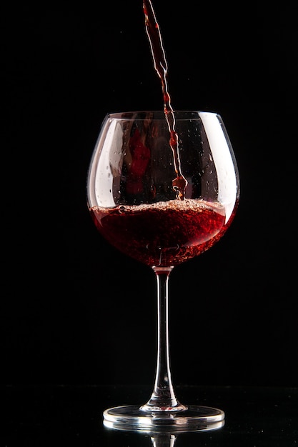 Bicchiere da vino vista frontale che viene versato con vino rosso su champagne xmas di colore nero