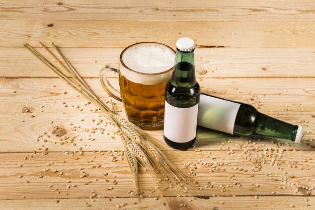 Bicchiere di birra con bottiglie e spighe di grano sulla tavola di legno