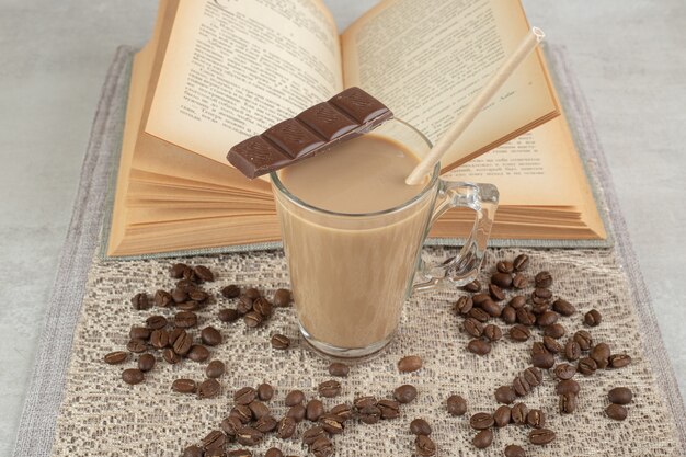 Bicchiere di caffè con cioccolato, libro e chicchi di caffè su tela