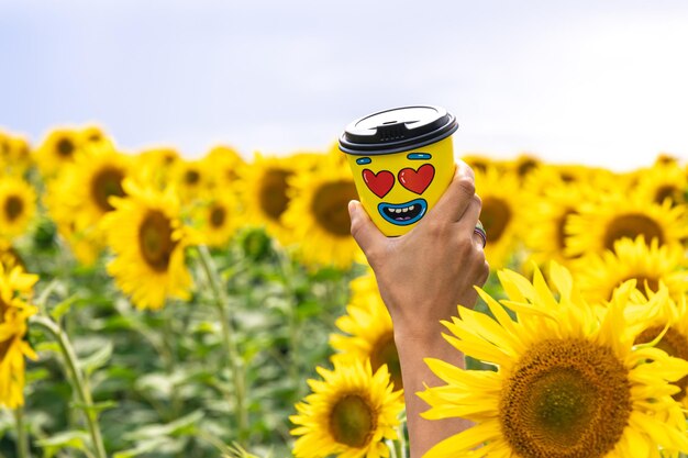 Bicchiere di caffè in una mano femminile sullo sfondo dei girasoli