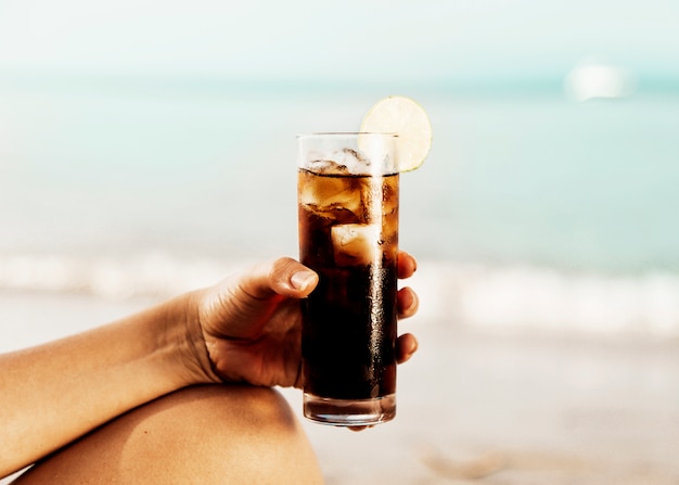 Bicchiere di coca cola con ghiaccio in mano sulla spiaggia