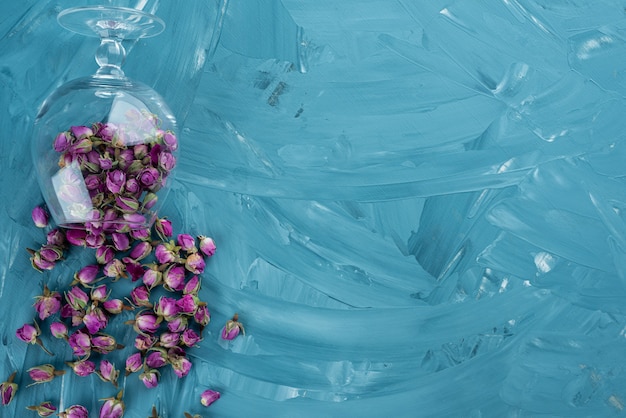 Bicchiere di rose viola essiccate sparse su sfondo blu.
