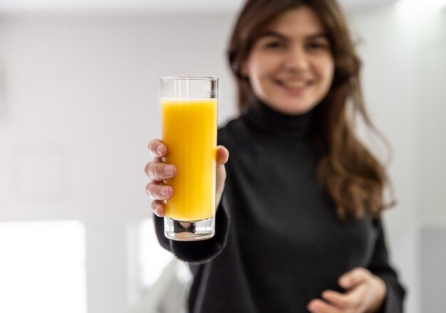 Bicchiere di succo d'arancia nelle mani di una giovane donna felice, sfondo sfocato.
