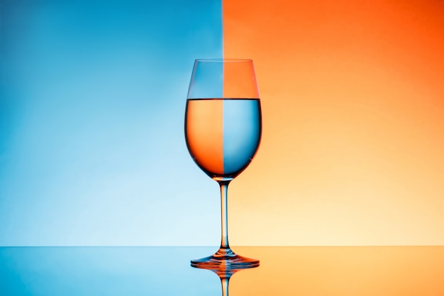 Bicchiere di vino con acqua sopra fondo blu ed arancio.