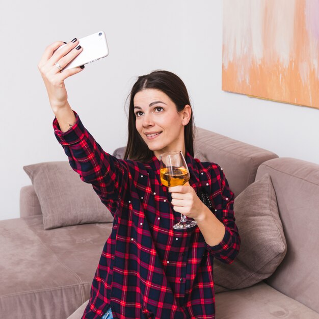 Bicchiere di vino della holding della giovane donna a disposizione prendendo selfie sul telefono cellulare