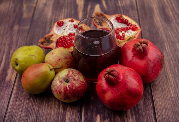 Bicchiere di vista frontale del succo di melograno con mele e pere melograni sulla parete di legno