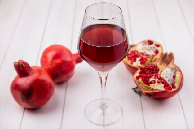 Bicchiere di vista frontale del succo di melograno con melograni sul muro bianco