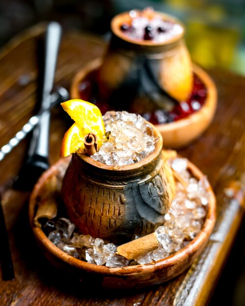 Bicchiere in legno di bevanda con stecca di zenzero di ghiaccio e fetta d'arancia