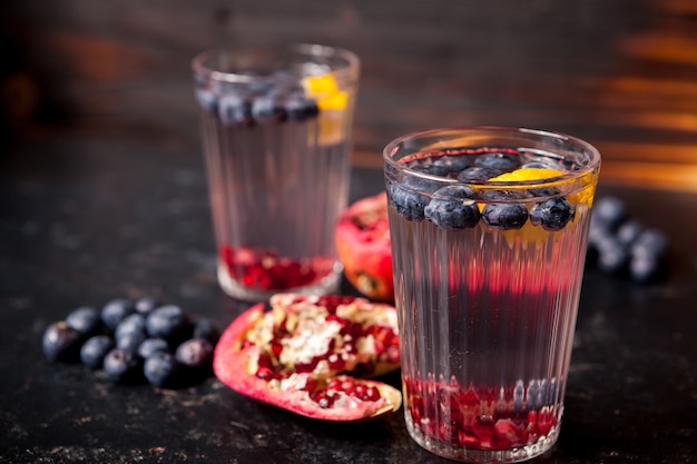 Bicchieri con acqua disintossicante a base di bacche organiche e melograno su fondo di legno vintage scuro