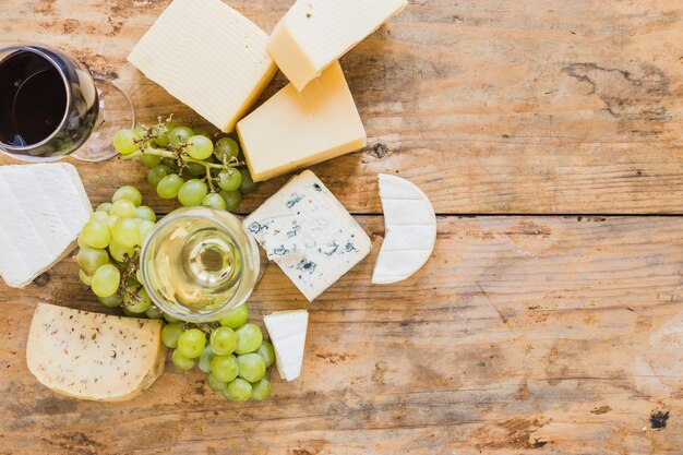 Bicchieri di vino con uva e varietà di blocchi di formaggio sulla scrivania in legno