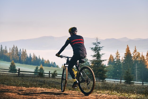 Bicicletta di guida del giovane sorridente sulla strada di montagna