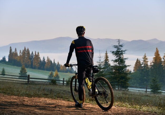 Bicicletta di guida del giovane sorridente sulla strada di montagna