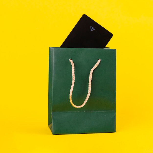 Biglietto da visita nero dentro il sacchetto della spesa di carta verde contro fondo giallo