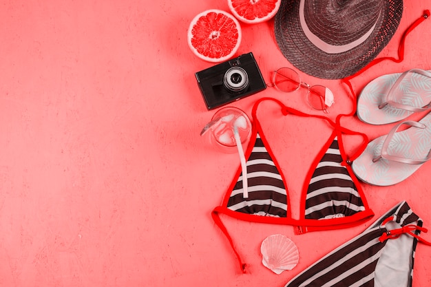 Bikini; cappello; telecamera; pinne; occhiali da sole; succo e pompelmo dimezzato su sfondo rosa strutturato