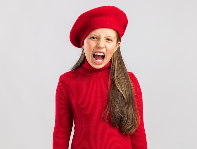 Bimba bionda preoccupata che indossa un berretto rosso che guarda davanti e urla isolata sul muro bianco con spazio per le copie