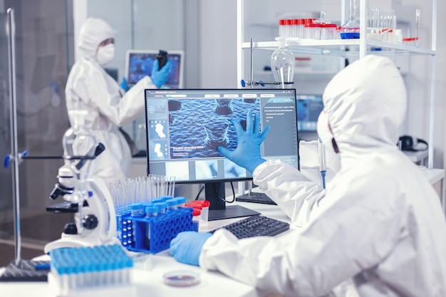 Biochimica in medicina che lavora in una struttura moderna per trovare una cura per il coronavirus vestita con una tuta. Ingegneri di laboratorio che conducono esperimenti per lo sviluppo di vaccini contro il virus covid19
