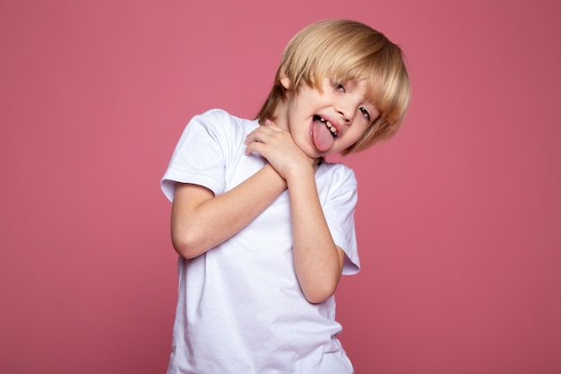 Bionda adorabile del ragazzo sveglio del bambino del ragazzo in maglietta bianca e sulla parete rosa