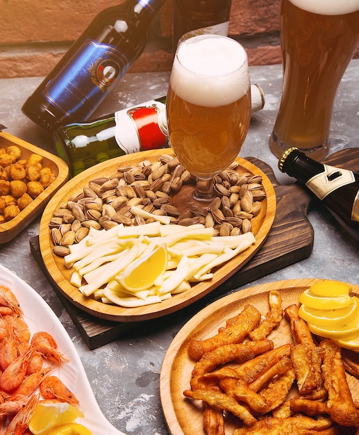 Birra chiara e spuntini sul tavolo di legno. Noci, scaglie di formaggio, pistacchi, creme