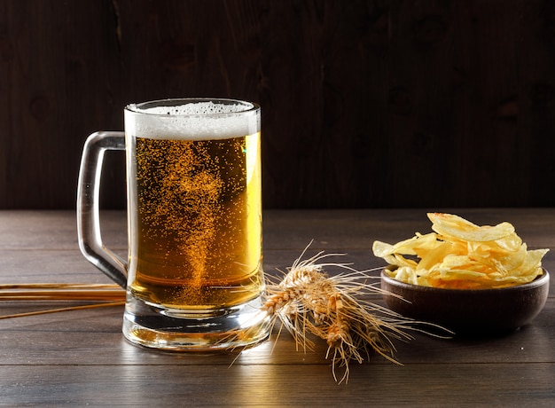 Birra in un bicchiere con spighe di grano, patatine fritte vista laterale su un tavolo di legno