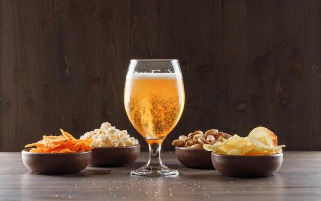 Birra in un bicchiere di calice con vista laterale di cibo spazzatura su un tavolo di legno