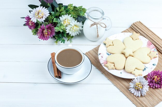 Biscotti a forma di cuore e stella di alta vista, fiori in tovaglietta con brocca di latte