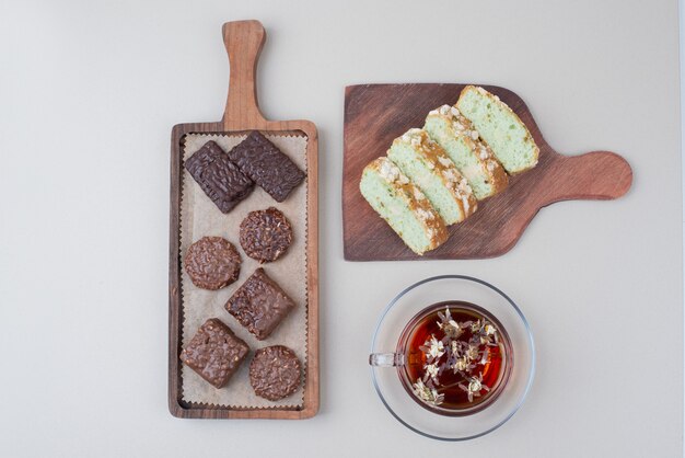 Biscotti al cioccolato, fette di torta al pistacchio e bicchiere di tè sulla superficie bianca.