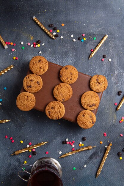 Biscotti al cioccolato gustosi vista dall'alto in lontananza sulla custodia marrone con candele da tè sullo sfondo grigio scuro biscotto biscotto tè dolce