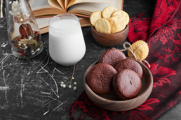 Biscotti al cioccolato in una tazza di legno con un bicchiere di latte.