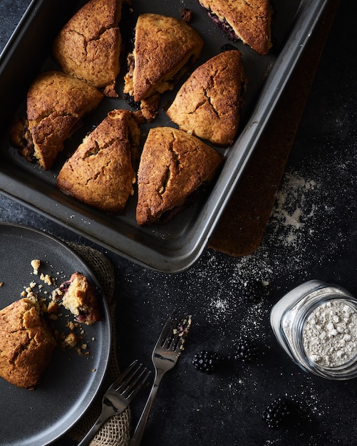 Biscotti appena sfornati in una padella e un biscotto mangiato per metà in un piatto su una superficie nera