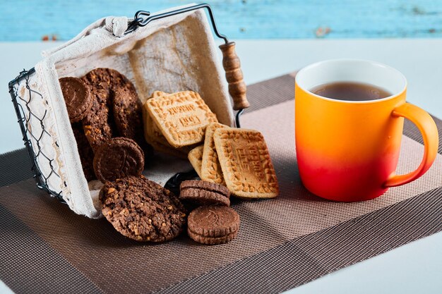 Biscotti assortiti, caramelle e una tazza di tè sulla superficie grigia.